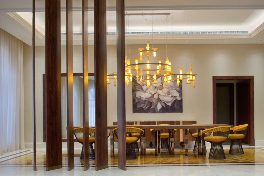 A dining room with yellow details completed with a wood dining table, some bespoke armchairs and a chandelier.