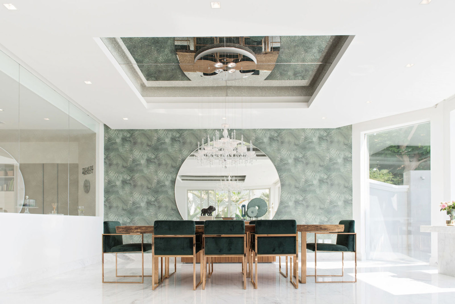 A dining room with white marble floor and green back wall furnished with bespoke upholstery and a center table.