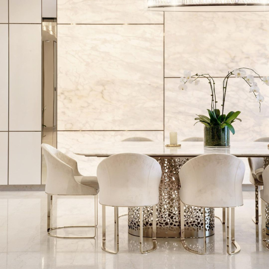 A dining room with white marble walls with a marble top dining table and white upholstery.