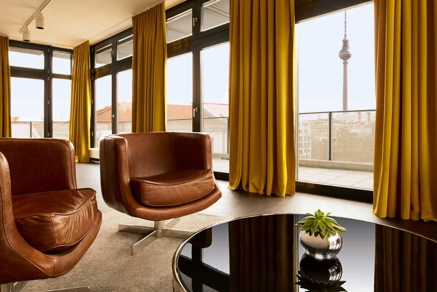 amano lounge area with 2 brown leather armchairs, yellow curtains on the windoes and a black center table. 