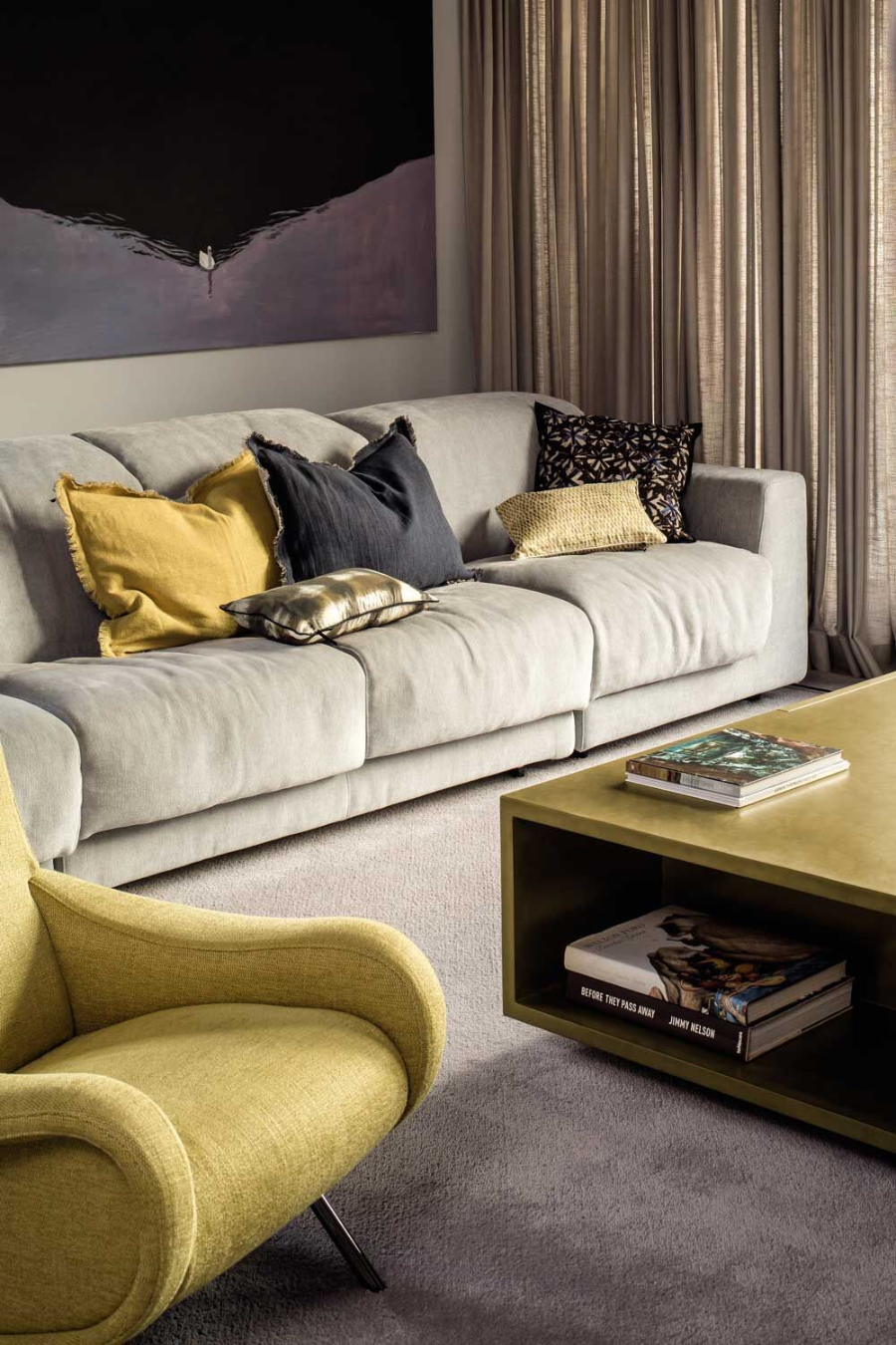 Apartment K 1.0 living room with a yellow armchair, a grey sofa with yellow pillows on talk, a white rug, and a square center table. 