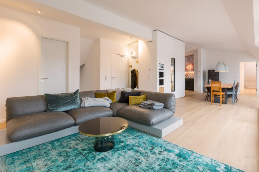 Penthouse Bogenhausen living room by BESPOKE with a blue rug, a grey sofa, and a dining table. 