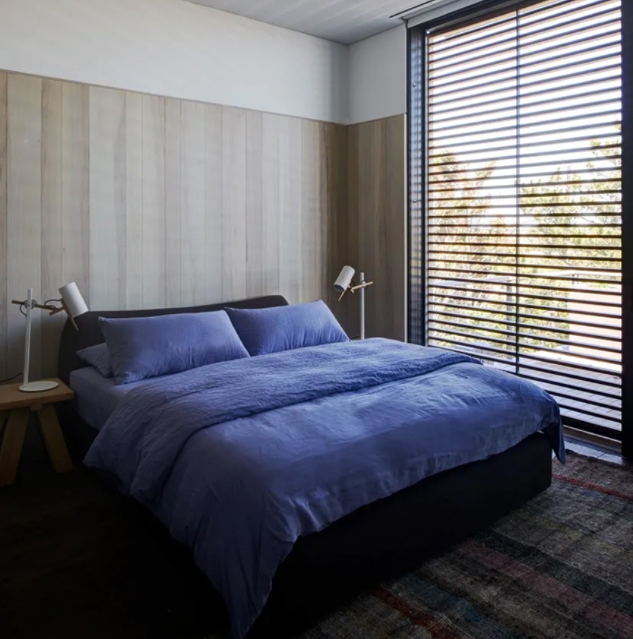 Interior Design Ideas with Yabu Pushelberg. This bedroom has a bed with blue sheets, two side tables in wood and a dark rug that covers all the room. 