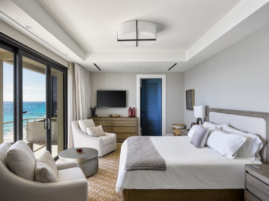Modern Contemporary Interior Design by Fleur-de-lis Interior Design. This bedroom has a white bed-frame with wood structure, two white armchairs, a coffee table in grey and covering all the room has a brown rug. 