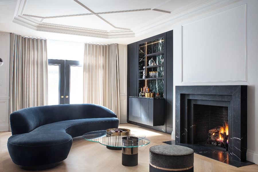 The Best Interior Design Ideas By Audax. This modern living room has a blue sofa, a glass coffee table, astool in grey ans a black marble fireplace. 