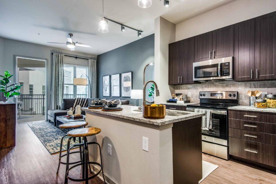 SJL Design Group: Interior Design In Texas. In this open space area there is a kitchen with dark wooden furniture, and a living room in gray tones.