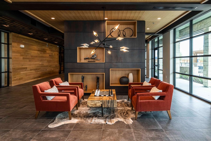 SJL Design Group: Interior Design In Texas. A living room in dark tones, there's a center table with four armchairs and a big suspension light over it.